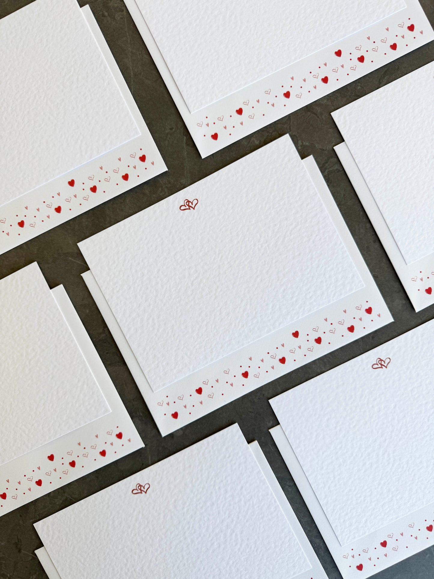 white correspondence cards illustrated with two linked love hearts, and a matching white envelope with heart confetti across the bottom