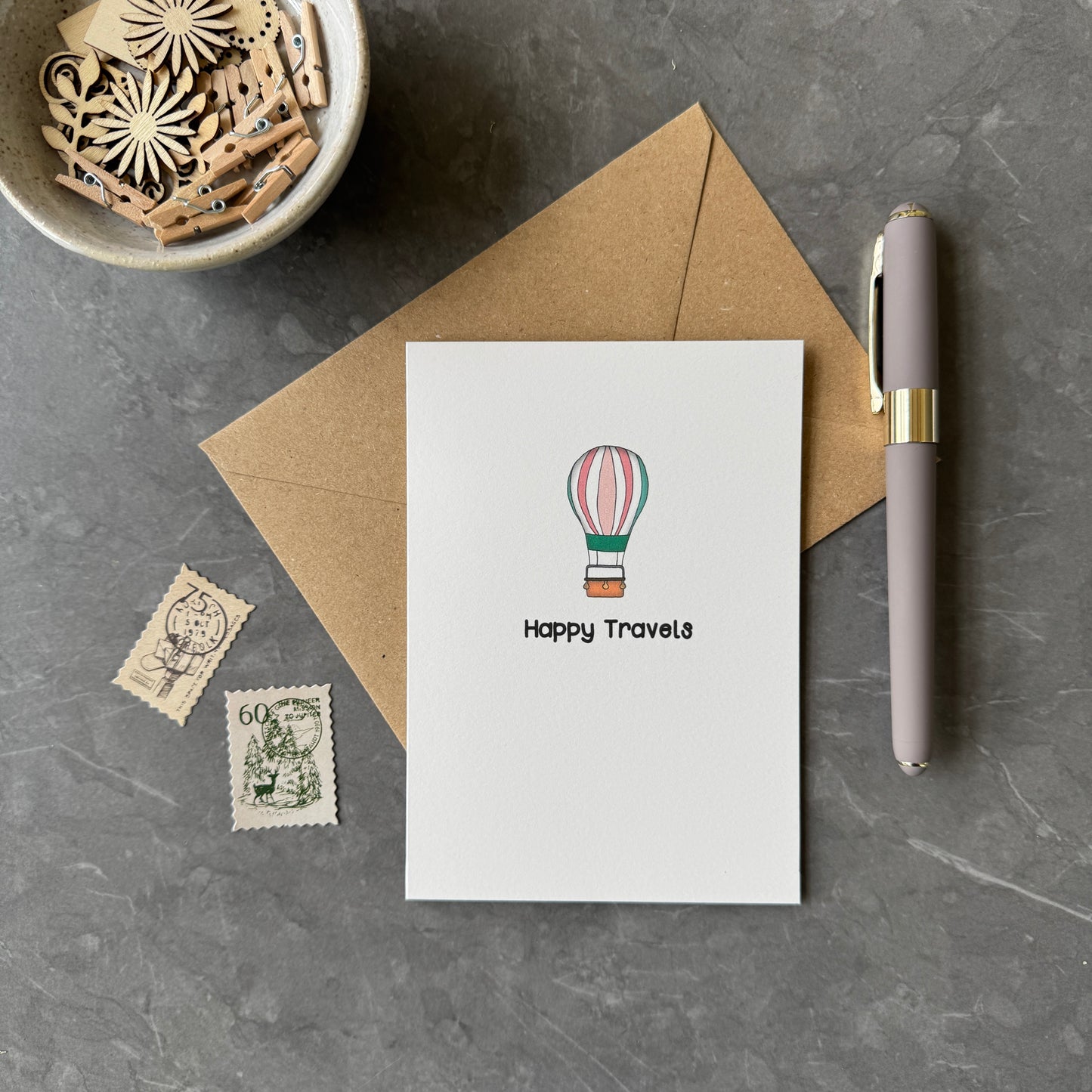 White greeting card with illustration of hot ari balloon and the words "Happy Travels" in a playful font.