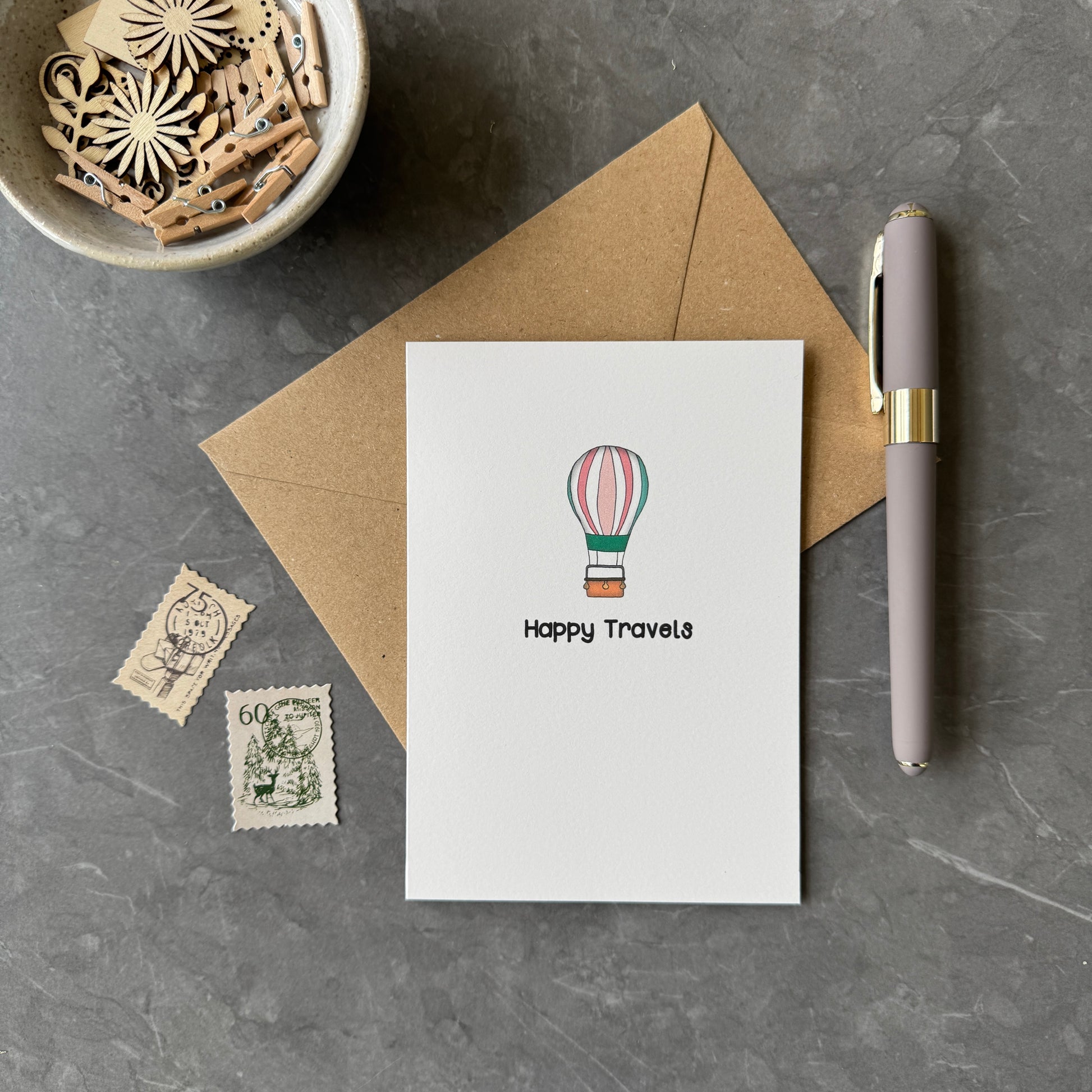 White greeting card with illustration of hot ari balloon and the words "Happy Travels" in a playful font.