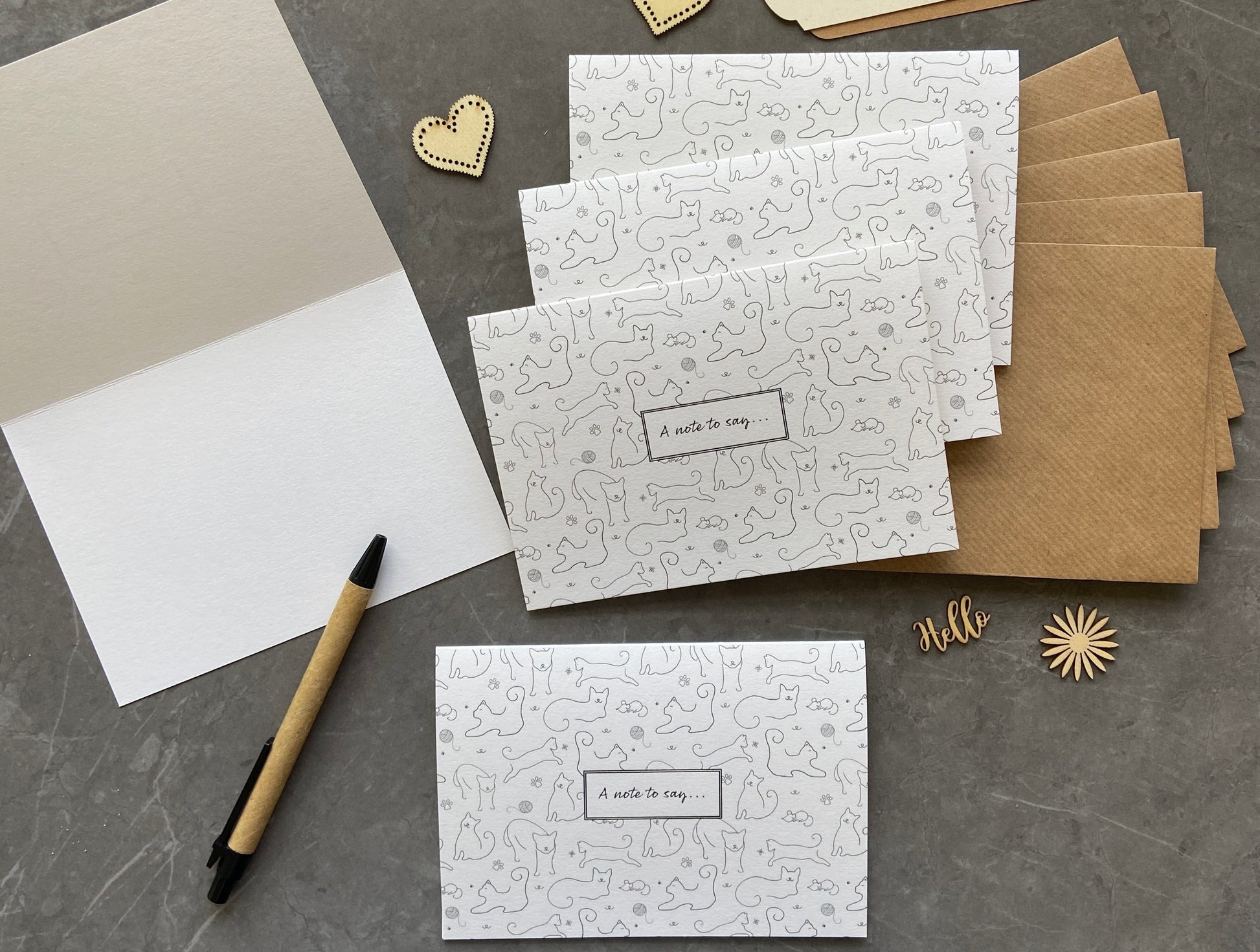 White note cards that are A6 in size and printed on smooth recycled card.  Each card shows a cat pattern with drawings of cats and other cat related motifs.  There is a white box in the centre with "A note to say" written in a script font